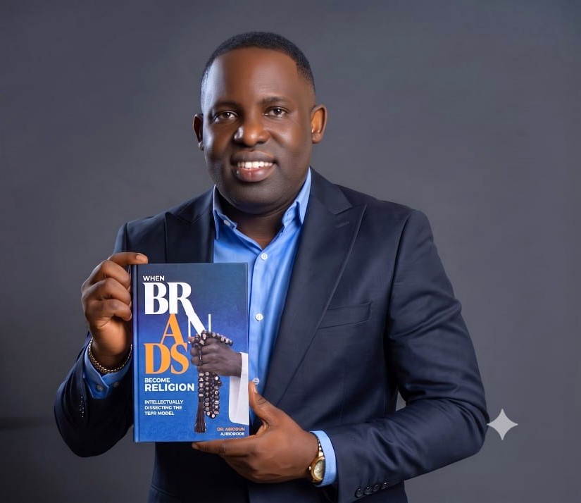 Dr. Abiodun Ajiborode holding When Brands Become Religion